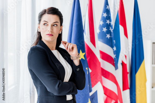 attractive diplomat looking away while standing near flags