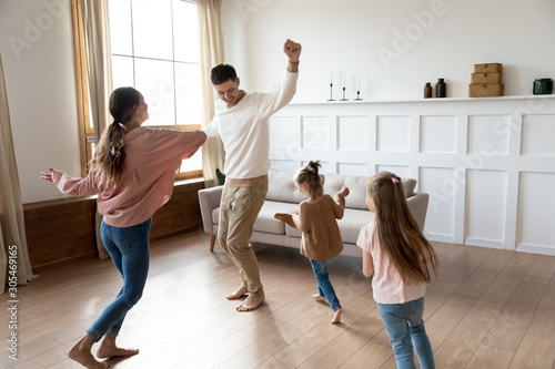 Funny active parents and children daughters dancing in living room