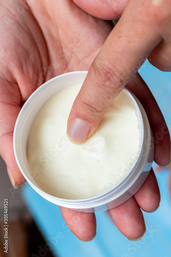 applying a white cosmetic cream on the girl hand from jar