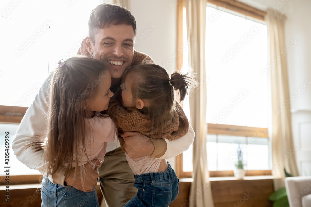 Loving young father hugging sweet small kids daughters at home Loving young father hugging sweet small kids daughters at home