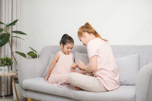 mom using pink nail polish to paint her cute daughter's nail to make her happier and prettier