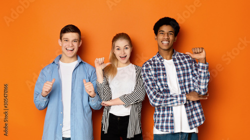 Diverse classmates pointing fingers at themselves, posing to camera photo