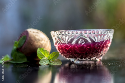 Detoxifying Beetroot extracted tincture in a glass bowl on black glossy surface with some raw fresh sliced beetroot vegetable with it used as a remedy for Inflammation in the kidney. Horizontal shot. photo