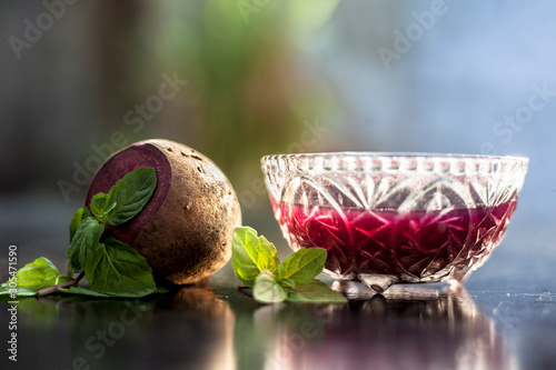 Detoxifying Beetroot extracted tincture in a glass bowl on black glossy surface with some raw fresh sliced beetroot vegetable with it used as a remedy for Inflammation in the kidney. Horizontal shot. photo