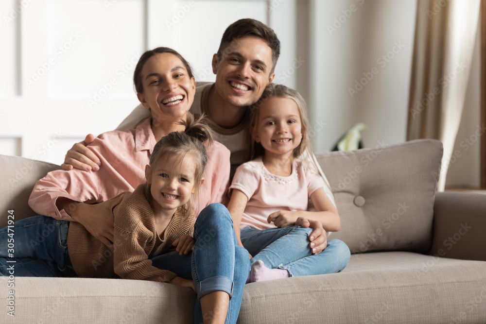 Smiling parents hug small kids daughters relaxing on couch, portrait Smiling parents hug small kids daughters relaxing on couch, portrait