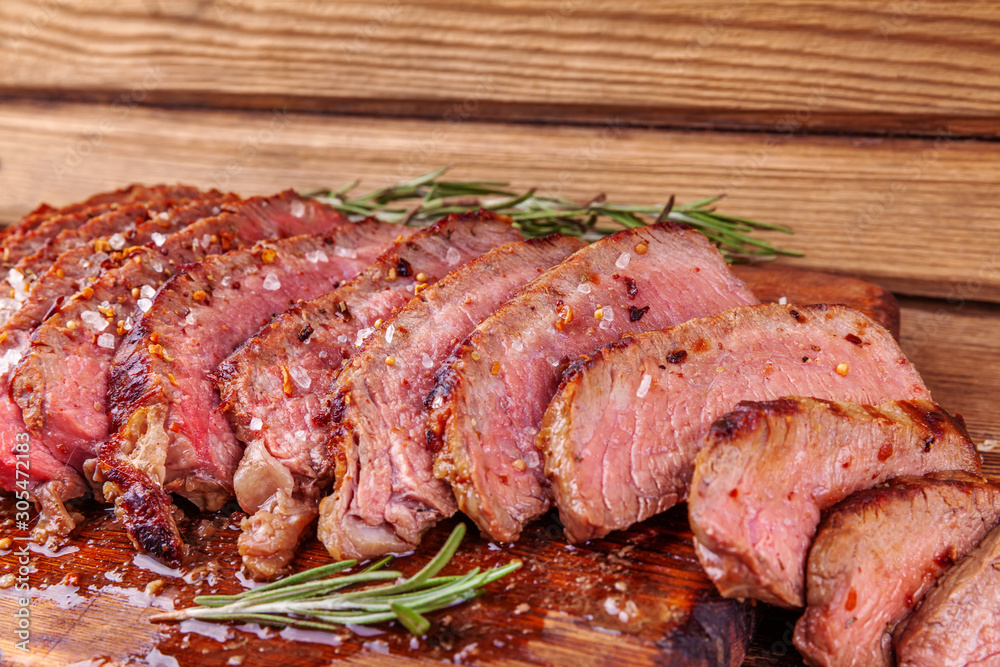 Chopped Grilled Steak Rib Eye on Rustic Cutting Board on Wooden Background. Juicy Medium Ribeye Steak with Spices and Rosemary. Concept of Delicious Meat Food