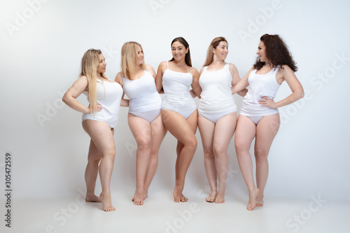 In love with myself. Portrait of beautiful plus size young women posing on white background. Happy smiling female models laughting together. Concept of body positive, beauty, fashion, style, feminism.