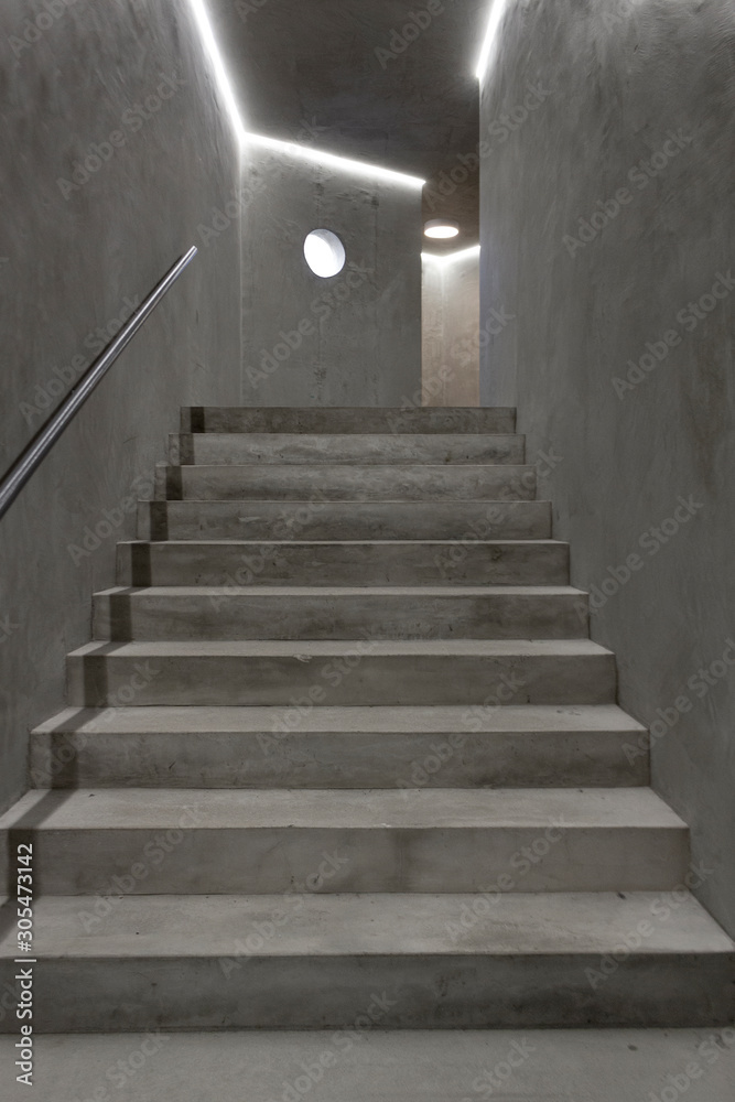 Empty modern reinforced concrete staircase with steel handrail and round window. Industrial style