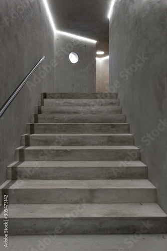 Empty modern reinforced concrete staircase with steel handrail and round window. Industrial style