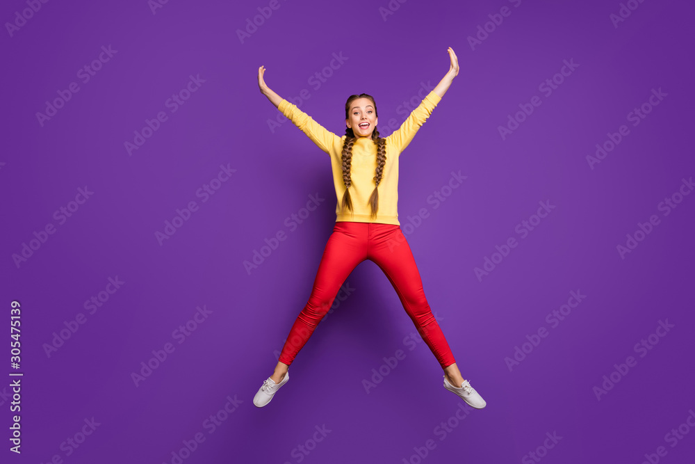 Full body photo of crazy youngster lady jumping high spending best free time spread hands star shape wear casual yellow pullover red trousers isolated purple color background