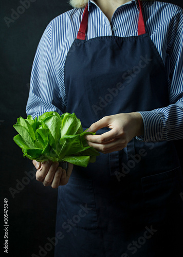 The cook in an apron holds a bunch of spinach in his hands. Healthy food. Vegetarian food. Dark background. Space for text.