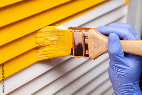 Closeup female hand in purple rubber glove with paintbrush painting natural wooden door with yellow paint. Concept creative design house interior. How to Paint Wooden Surface. Selected focus photo