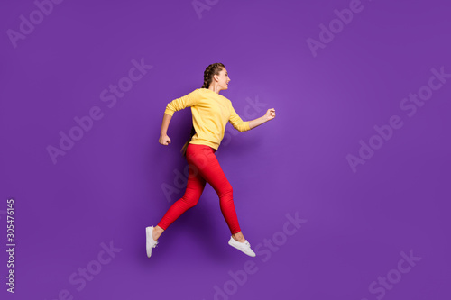 Full length profile photo of funny millennial lady jumping high rushing sale shopping speed running wear casual yellow pullover red trousers isolated purple color background
