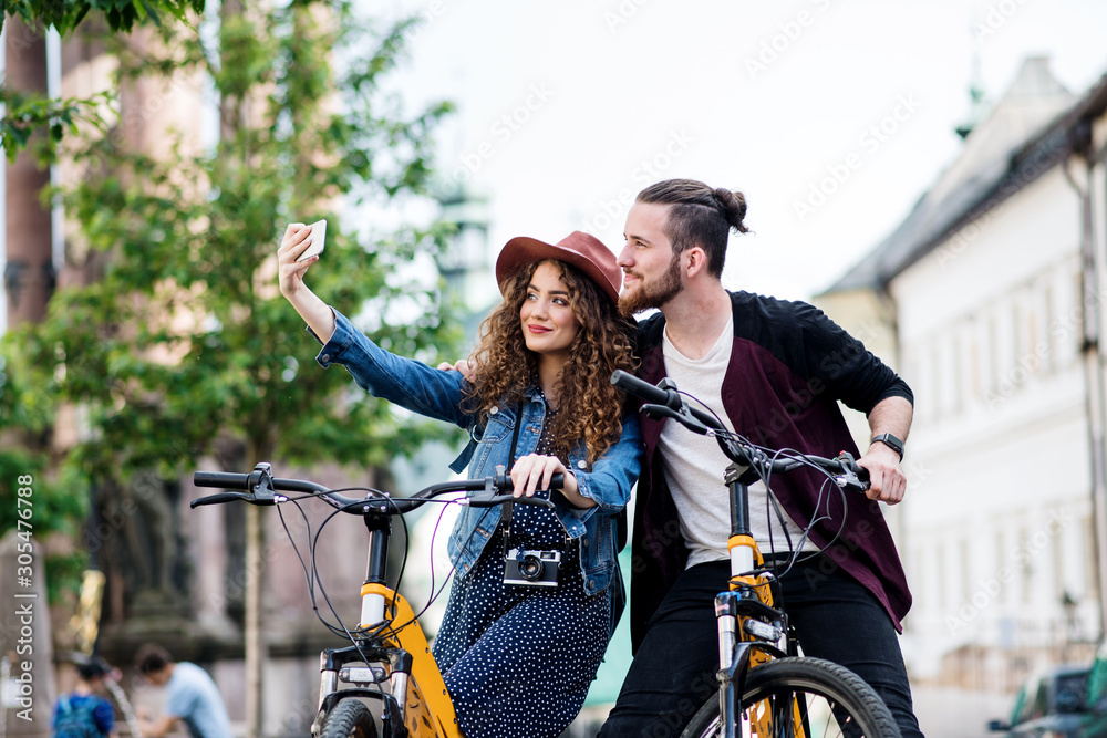 Obraz premium Young couple with electric scooters and smartphone in town, taking selfie.