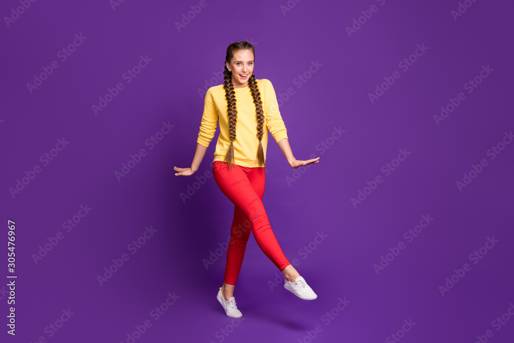 Full length photo of funny millennial lady walking down street long braids amazing warm sunny day wear casual yellow pullover red trousers isolated purple color background