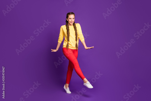 Full length photo of funny millennial lady walking down street long braids amazing warm sunny day wear casual yellow pullover red trousers isolated purple color background