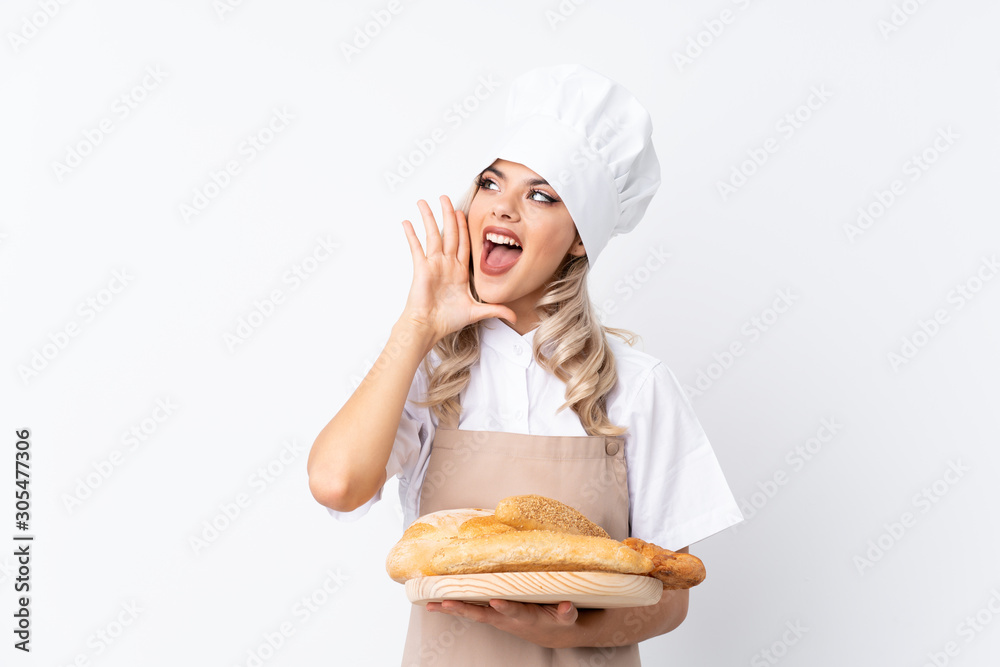 Teenager girl in chef uniform. Female baker holding a table with several breads over isolated white background shouting with mouth wide open Teenager girl in chef uniform. Female baker holding a table with several breads over isolated white background shouting with mouth wide open