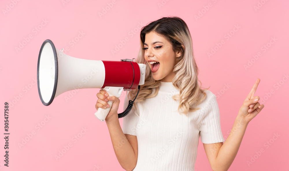 Teenager girl over isolated pink background shouting through a megaphone Teenager girl over isolated pink background shouting through a megaphone
