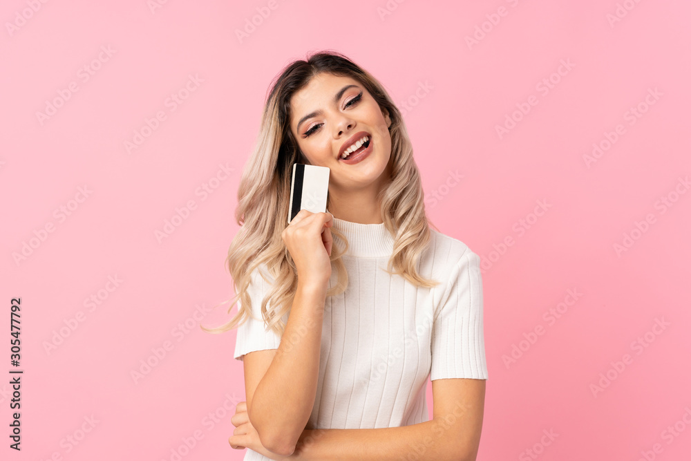 Teenager girl over isolated pink background holding a credit card Teenager girl over isolated pink background holding a credit card
