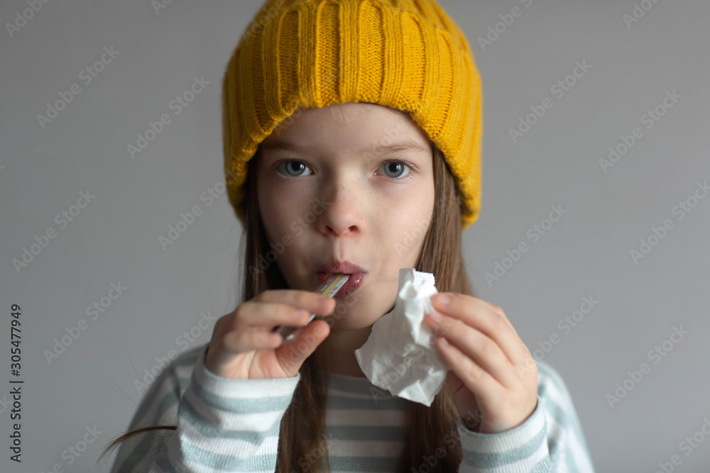 portrait of a little sad unhappy girl in a hat, suffering from the flu virus ,runny nose and headache, measures the temperature with a thermometer, looks at the camera portrait of a little sad unhappy girl in a hat, suffering from the flu virus ,runny nose and headache, measures the temperature with a thermometer, looks at the camera