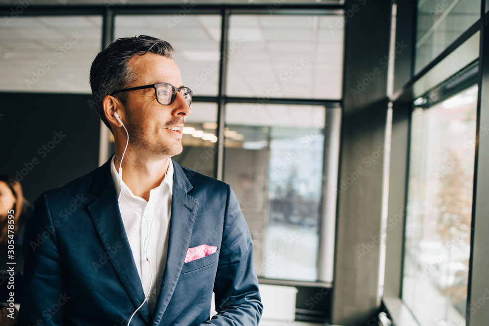Smiling businessman wearing headphones looking away in office Smiling businessman wearing headphones looking away in office