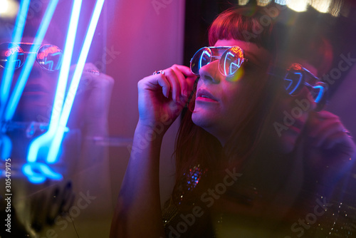 girl with sunglasses and fringe looking at neon lights