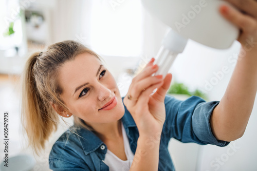 Young woman indoors at home  changing light bulb.