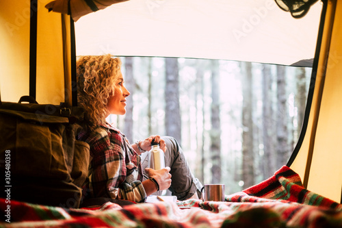 Alternative free beautiful caucasian people enjoy the outdoor nature leisure activity alone inside a tent with forest outside - vacation time and travel adventure lifestyle woman #305480358