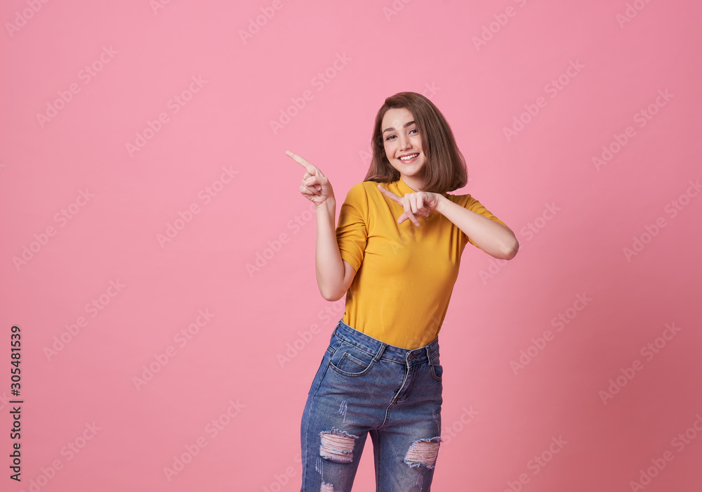 Happy young woman standing with her finger pointing isolated over pink banner background with copy space. Happy young woman standing with her finger pointing isolated over pink banner background with copy space.