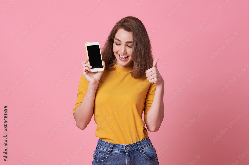 Portrait of happy young woman showing at blank screen mobile phone and hand gesture good isolated over pink background.