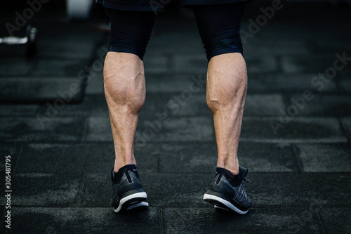 trained legs with muscular calves in sneakers in training gym during hard fitness and crossfit workout