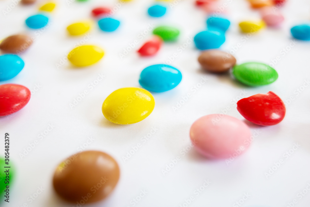 Scattered multi-colored small round candies. Chocolate dragees in multi-colored glaze on a white background. Scattered multi-colored small round candies. Chocolate dragees in multi-colored glaze on a white background.