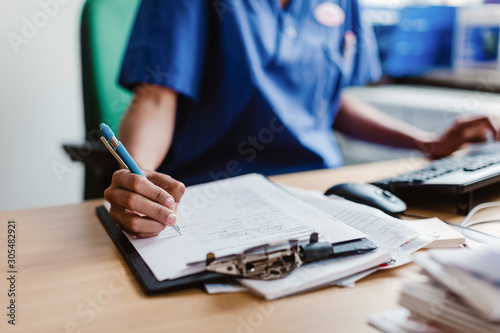 Midsection of nurse writing medical report while sitting at desk in clinic photo