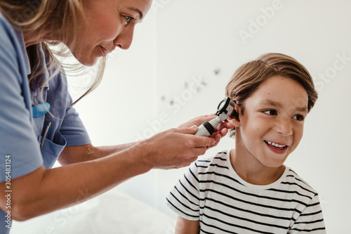 Doctor examining boy's ear with otoscope in medical examination room photo