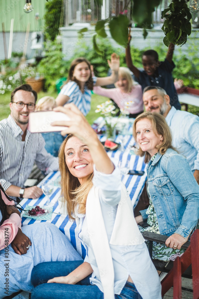 Woman taking selfie with family and friends at dining table in garden party Woman taking selfie with family and friends at dining table in garden party