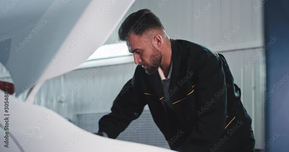 Attractive guy portrait in front of the camera mechanic in a service auto working concentrated fixing the car engine and get sweating Attractive guy portrait in front of the camera mechanic in a service auto working concentrated fixing the car engine and get sweating