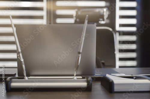 Modern office workplace. Business laptop in work place for chief, boss or other employees. Notebook on work table. Office large corporation. Light through half open blinds