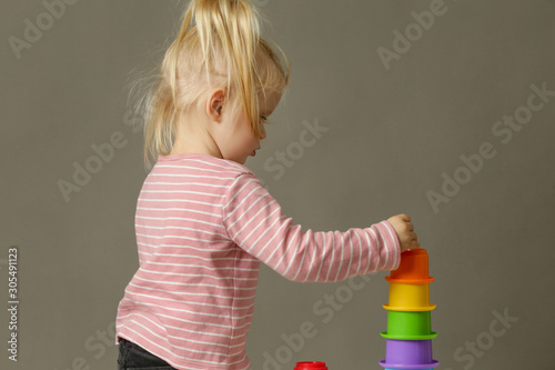Studio shot of a toddler playing with colorful plastic cups, motor skill development. These activities for toddlers will get little hands and fingers ready for later-developing skills.
