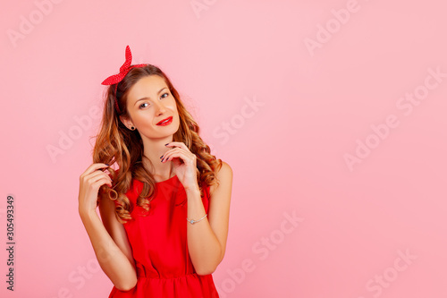Portrait of a cheerful рыжие волосы pin-up girl in красном платье and looking в камеру over pink background. Copy space area for advertise, slogan or text message 