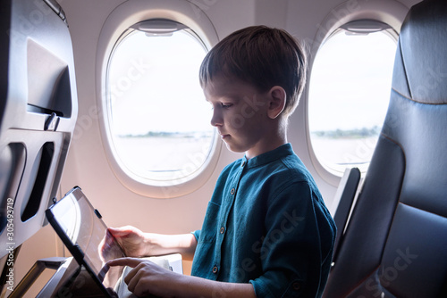Cute six years old boy, playing on tablen in aircraft on boar, traveling on vacation with parents and siblings photo