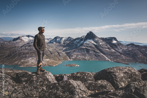 Healthy young man happy traveler tourist standing on top of a rock high in the mountains, enjoying the natural beauty in the morning light. Scandinavia and Arctic background with snow and glacier