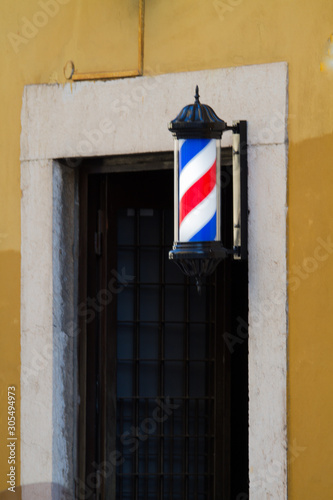 Barber shop pole by the entrance lights up in the dark. © Giordano