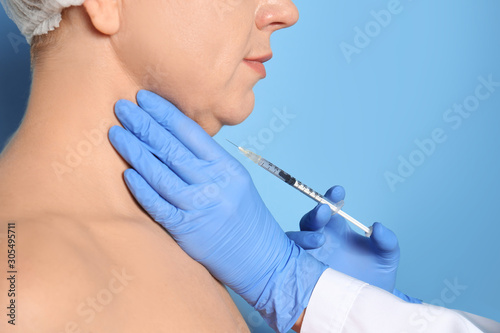Mature woman with double chin receiving injection on blue background  closeup