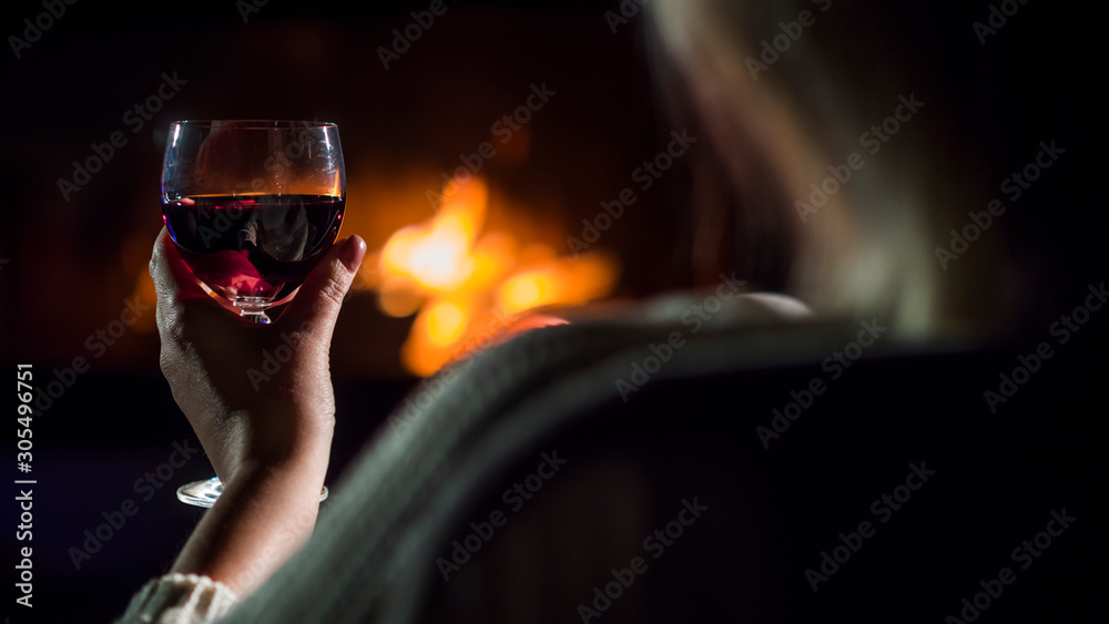 Rear view of Woman drinking red wine while sitting by the fireplace, rear view