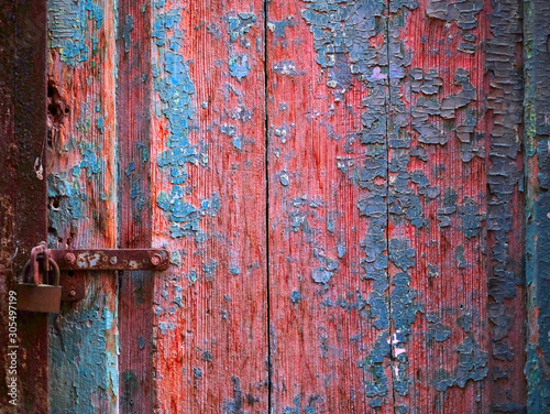 Vintage wooden door with flaking blue paint, locked with a rusty tab and a padlock.