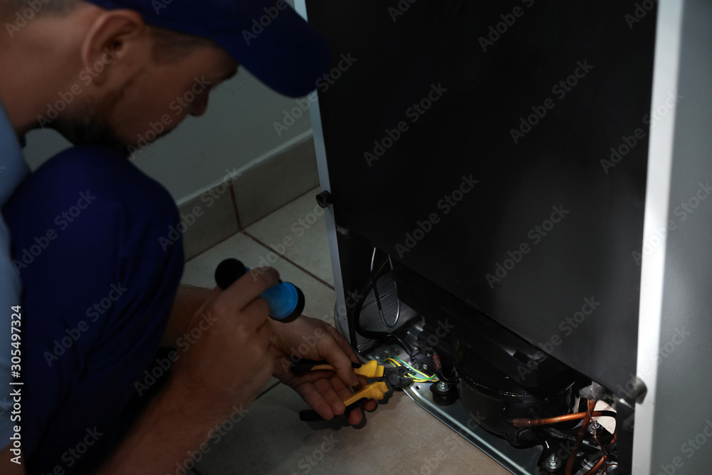 Electrician with flashlight fixing refrigerator indoors, closeup Electrician with flashlight fixing refrigerator indoors, closeup
