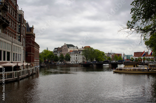 View of canal  boats  historical and traditional buildings in Amsterdam. It is a summer day with cloudy sky.