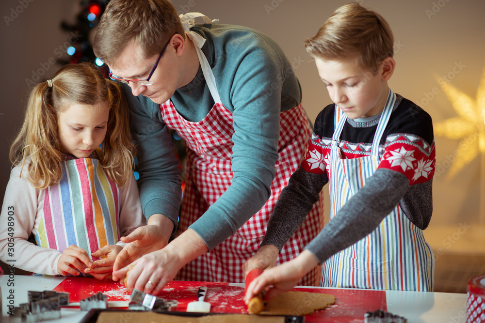 Fototapeta premium Happy father with his children bakes ginger cookies for Christmas with christmas tree on background