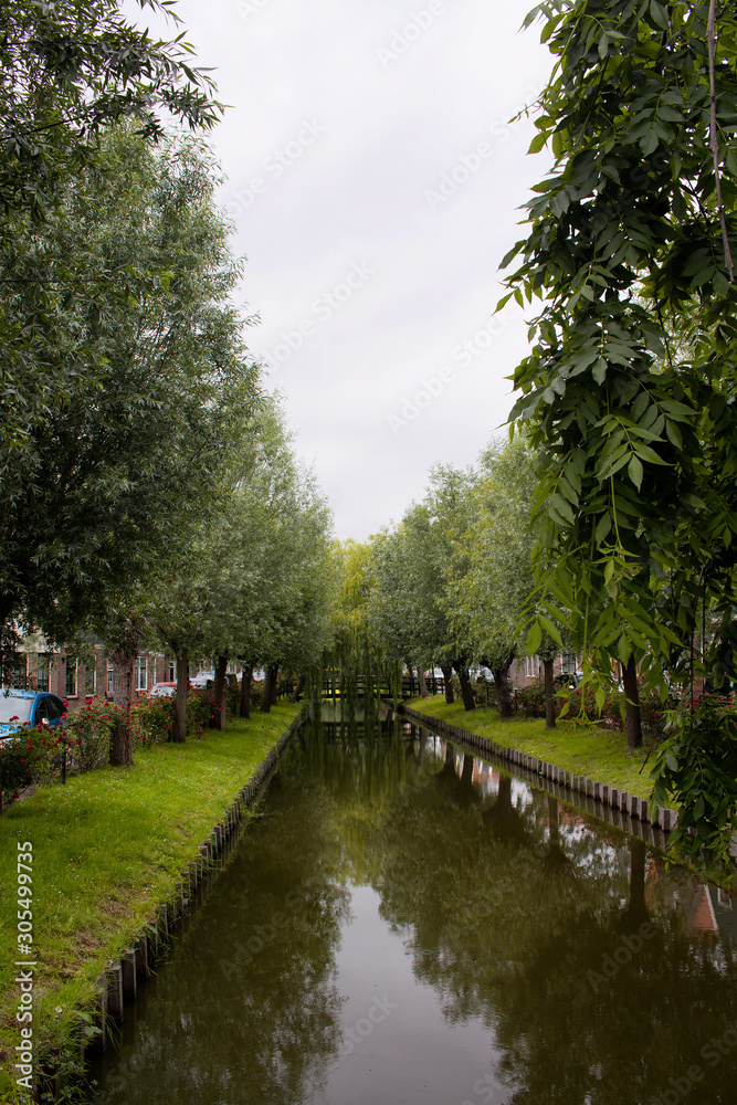 View of a river and trees in Voldendam. It is a Dutch town, northeast of Amsterdam. It’s known for its colorful wooden houses and the old fishing boats.