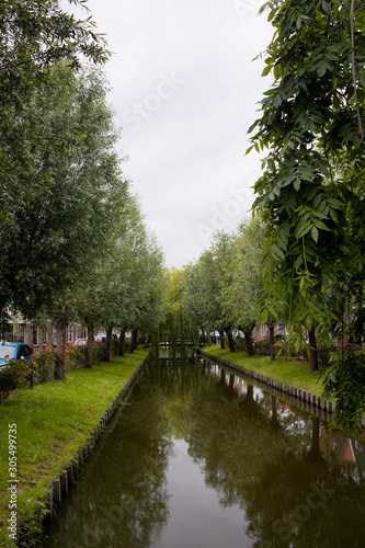 View of a river and trees in Voldendam. It is a Dutch town, northeast of Amsterdam. It’s known for its colorful wooden houses and the old fishing boats.